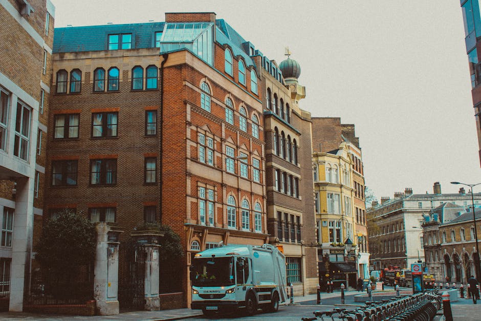 A wide-angle view of a street scene outside a white multi-storey residential building with numerous uniformly sized windows and black iron railings, typical of a London townhouse. In the foreground, t